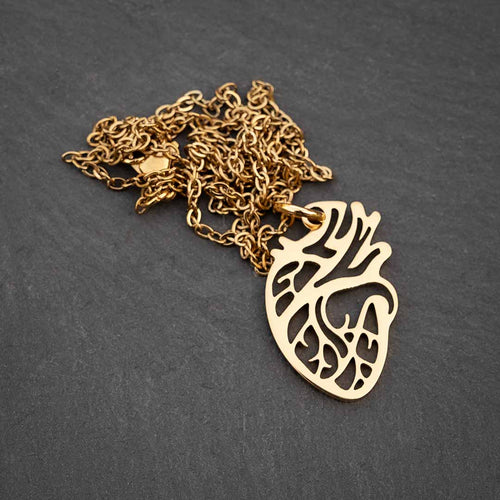 Gold-tone die-cut anatomical heart pendant on a cable chain, laid on a dark slate surface