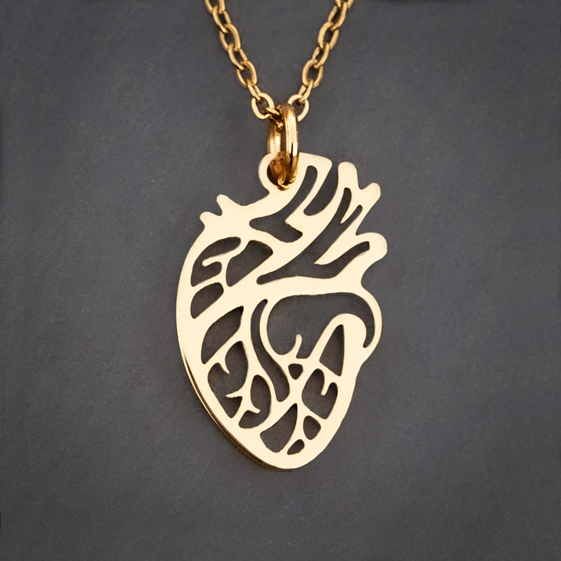 Close-up of a gold-tone anatomical heart pendant showing open-cutout chamber and vessel detailing