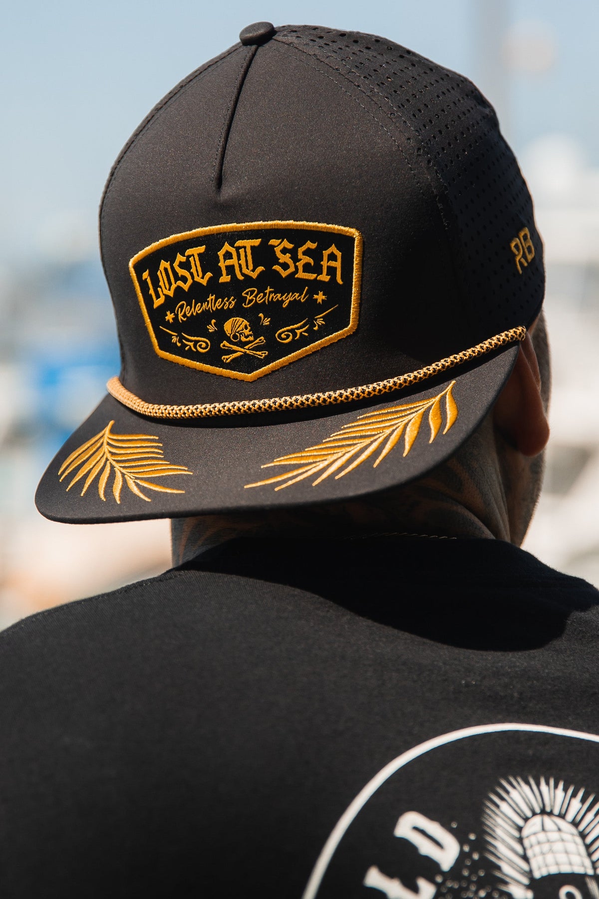 Lost At Sea BLACKOUT Snapback: black cap with gold-colored LOST AT SEA patch, rope trim and leaf embroidery on brim, worn backward.