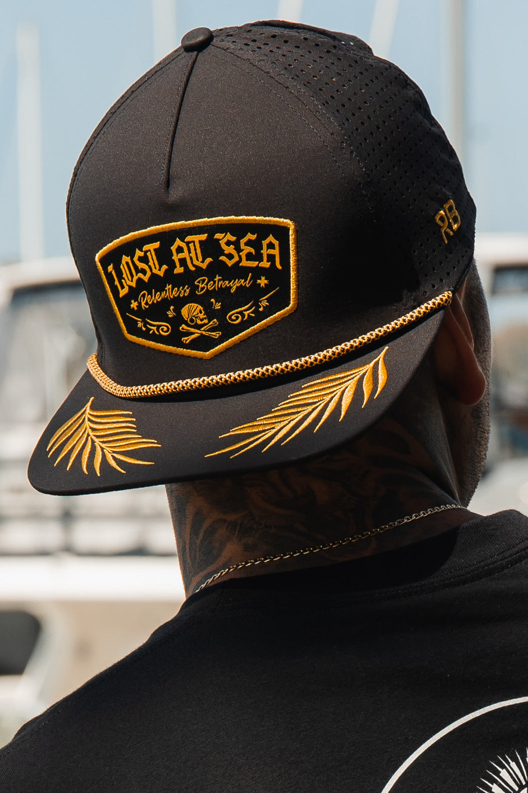 Lost At Sea BLACKOUT Snapback: black cap with gold-colored LOST AT SEA patch, rope trim and leaf embroidery on brim, worn backward.