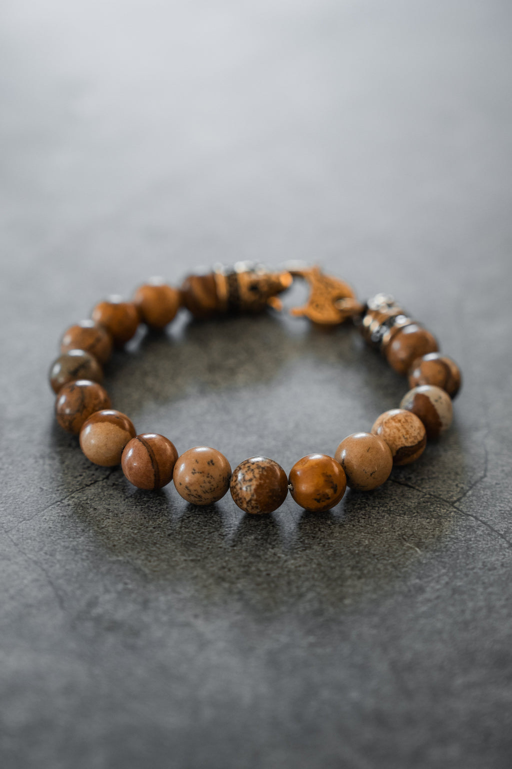 Desert Storm Gemstone GOLD Ed. Bracelet: brown marbled round beads with decorative gold-tone clasp, full bracelet on gray surface.