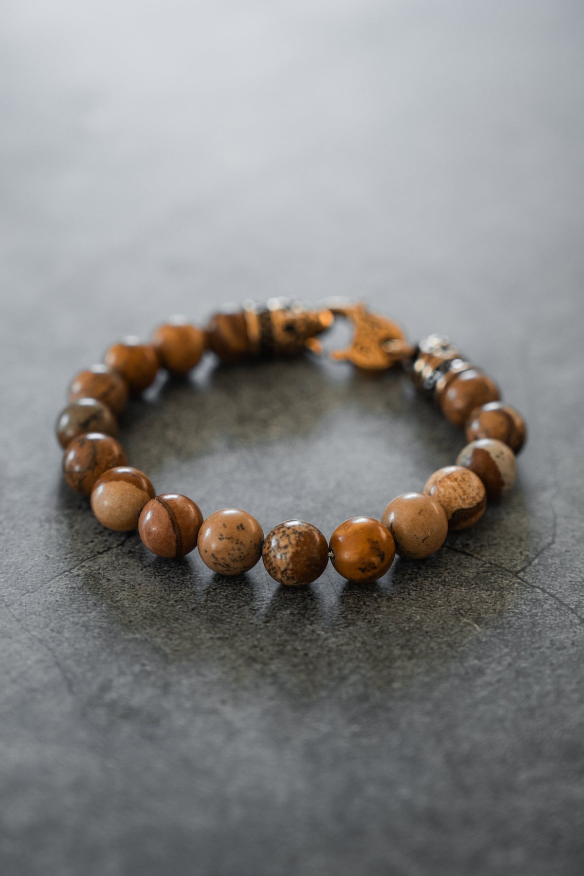 Desert Storm Gemstone GOLD Ed. Bracelet: brown marbled round beads with decorative gold-tone clasp, full bracelet on gray surface.