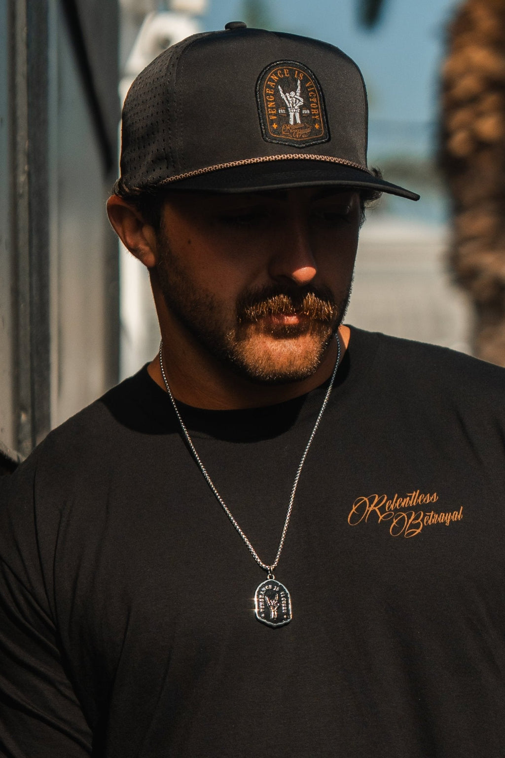 Vengeance Necklace: black shield-shaped pendant with skeletal hand and VENGEANCE IS VICTORY lettering, worn on a model.