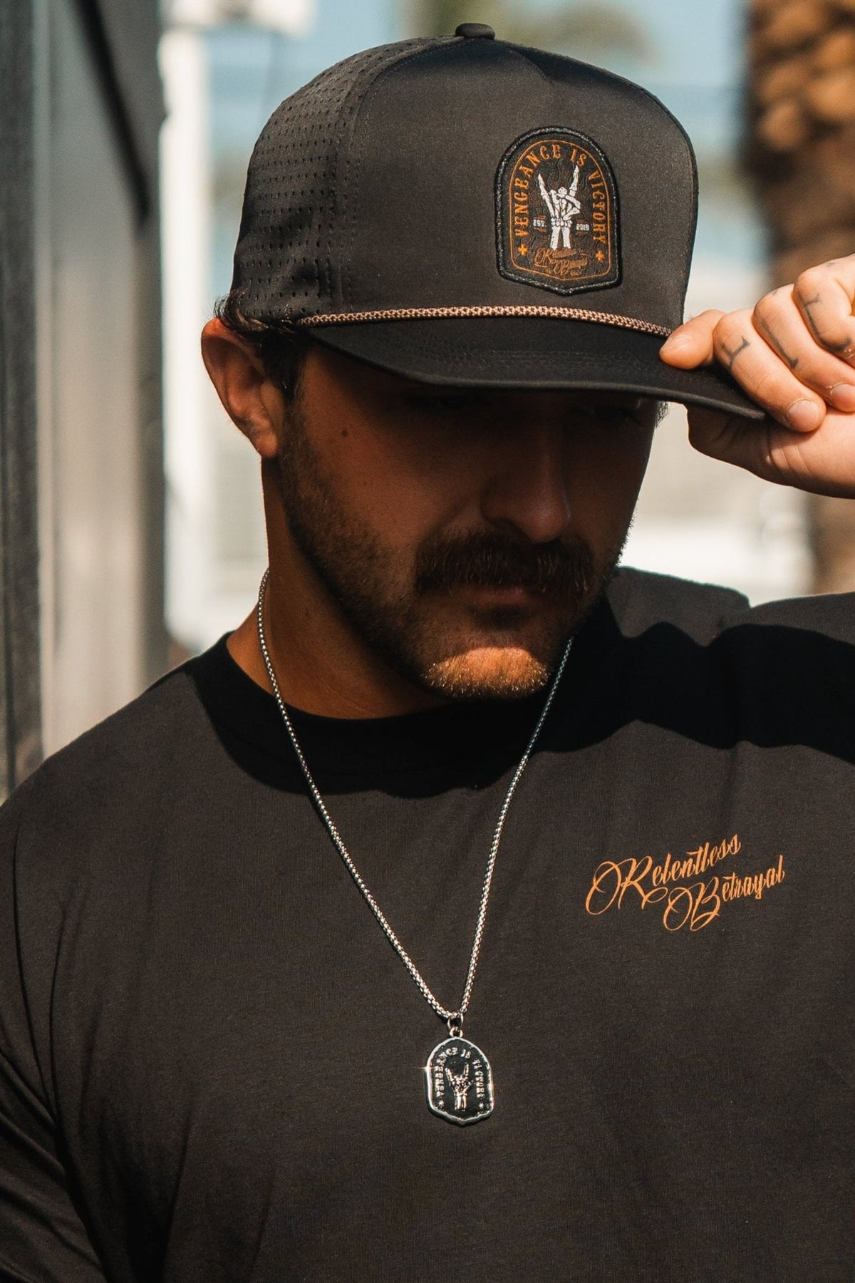 Vengeance Necklace: black shield-shaped pendant with skeletal hand and VENGEANCE IS VICTORY lettering, worn on a model.