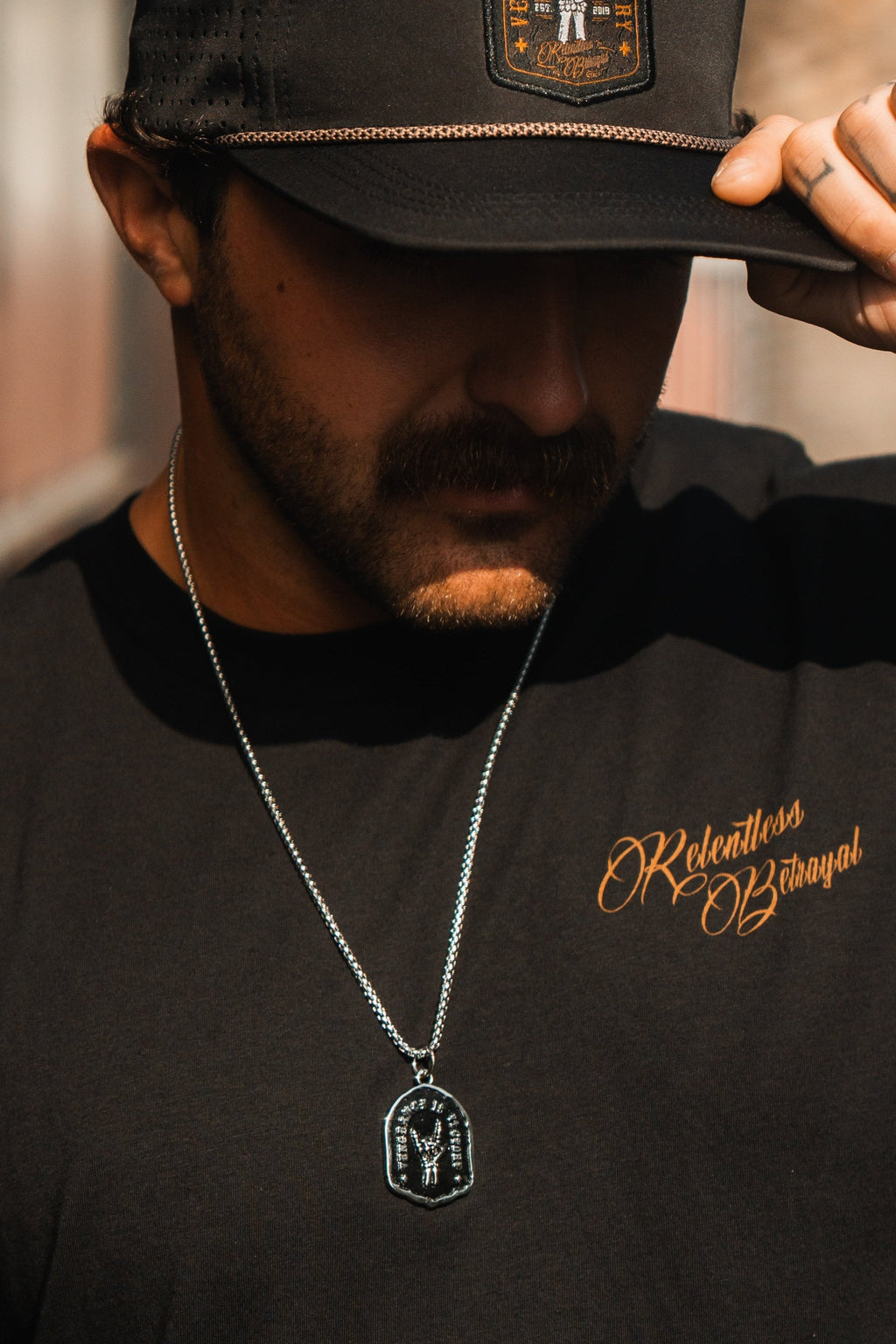 Vengeance Necklace: black shield-shaped pendant with skeletal hand and VENGEANCE IS VICTORY lettering, worn on a model.