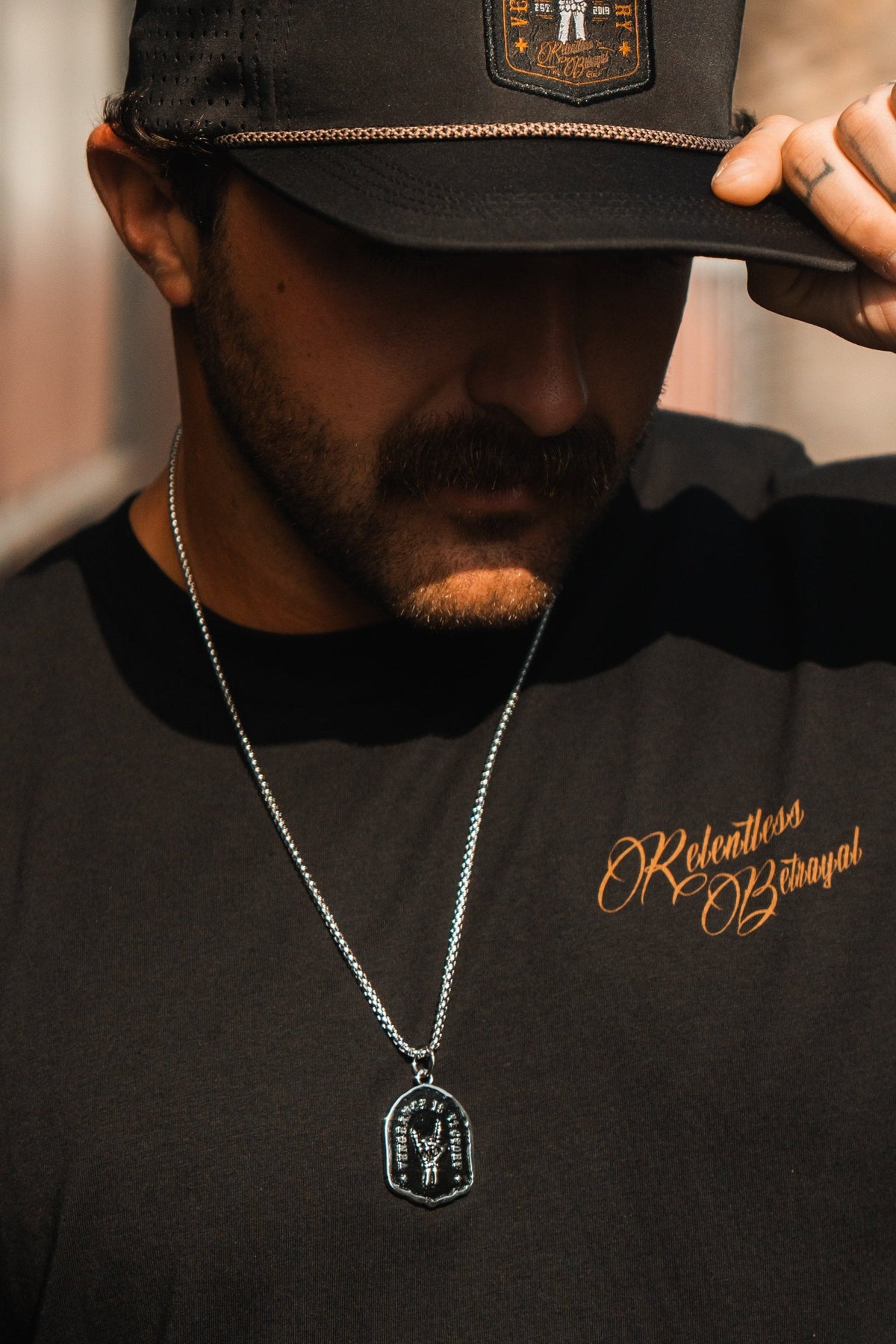 Vengeance Necklace: black shield-shaped pendant with skeletal hand and VENGEANCE IS VICTORY lettering, worn on a model.