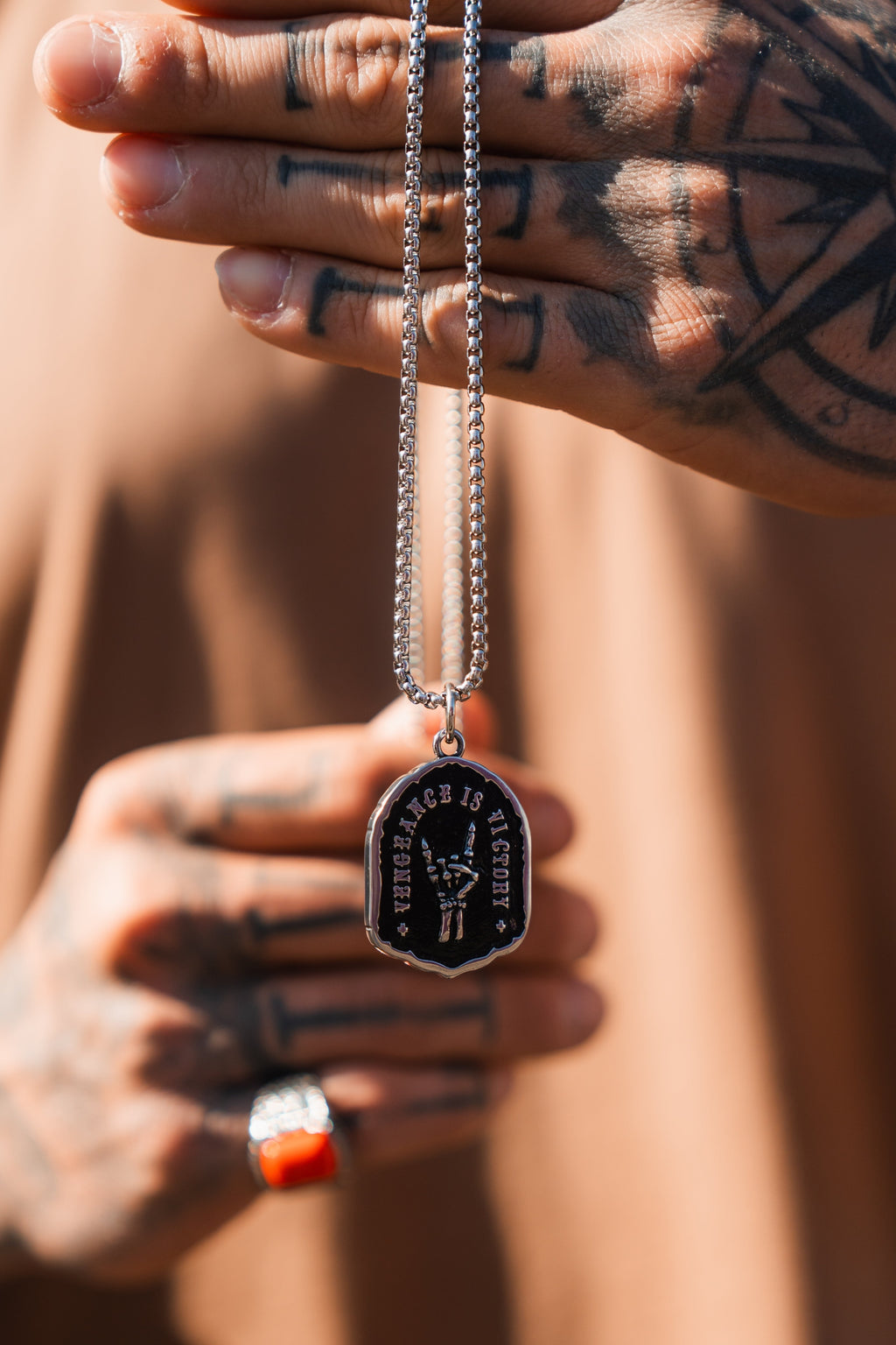 Vengeance Necklace: black shield-shaped pendant with skeletal hand and VENGEANCE IS VICTORY lettering, held by its chain.