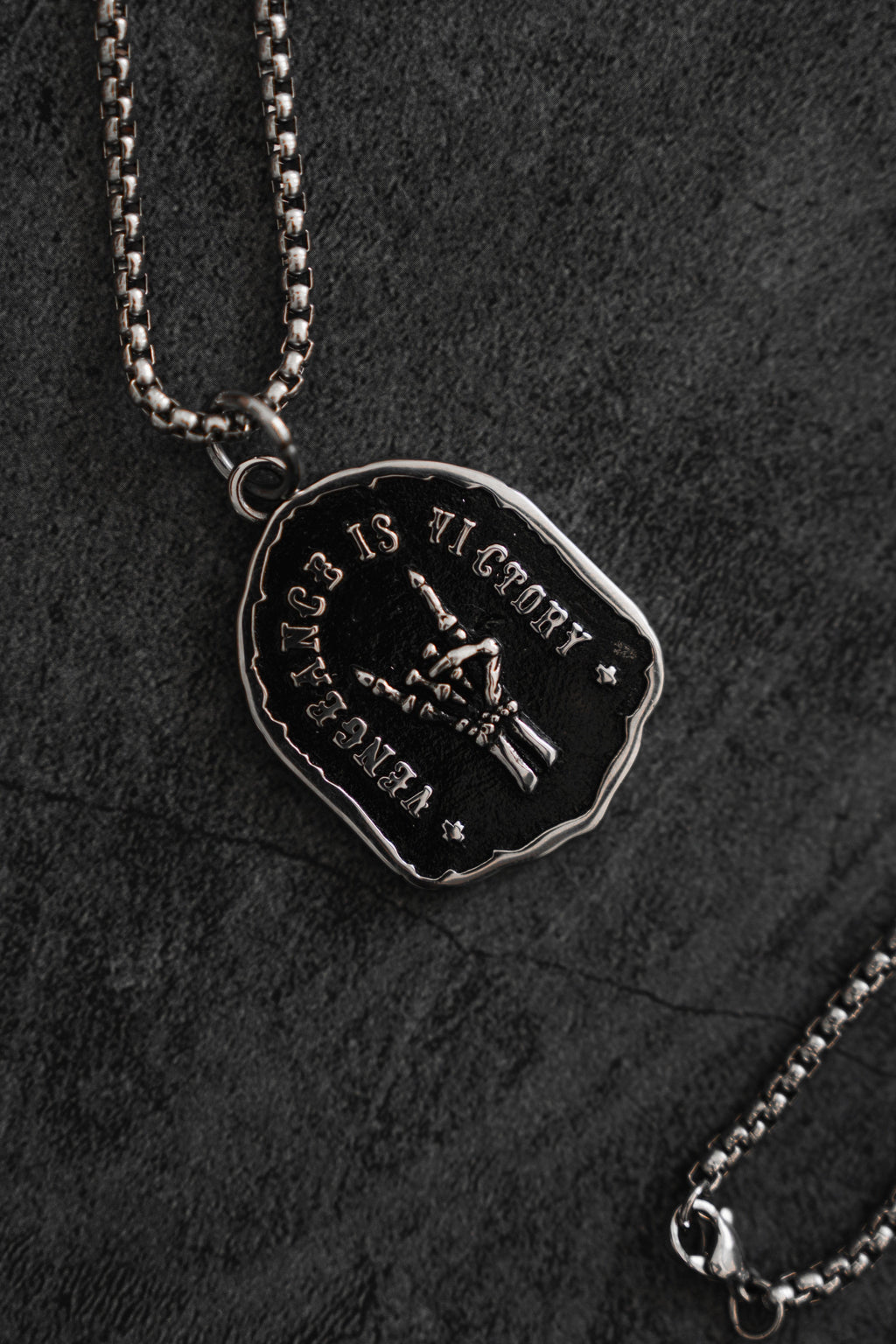 Vengeance Necklace: black shield-shaped pendant with skeletal hand and VENGEANCE IS VICTORY lettering, front with chain and clasp.