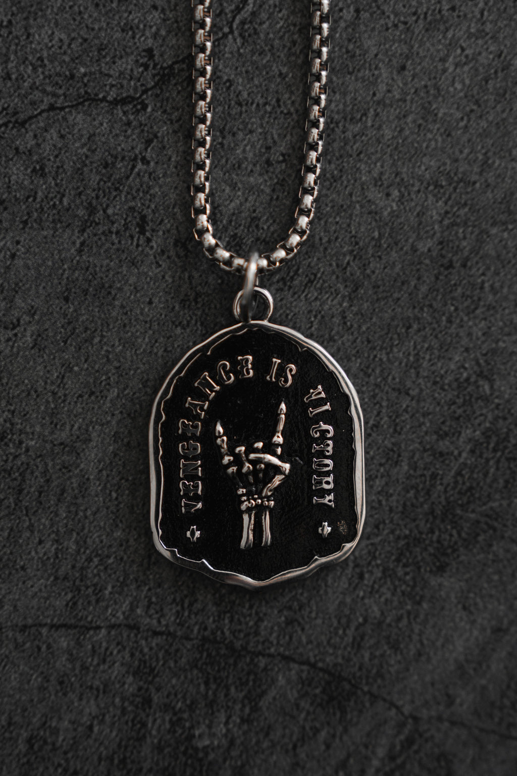 Vengeance Necklace: black shield-shaped pendant with skeletal hand and VENGEANCE IS VICTORY lettering, front product view.