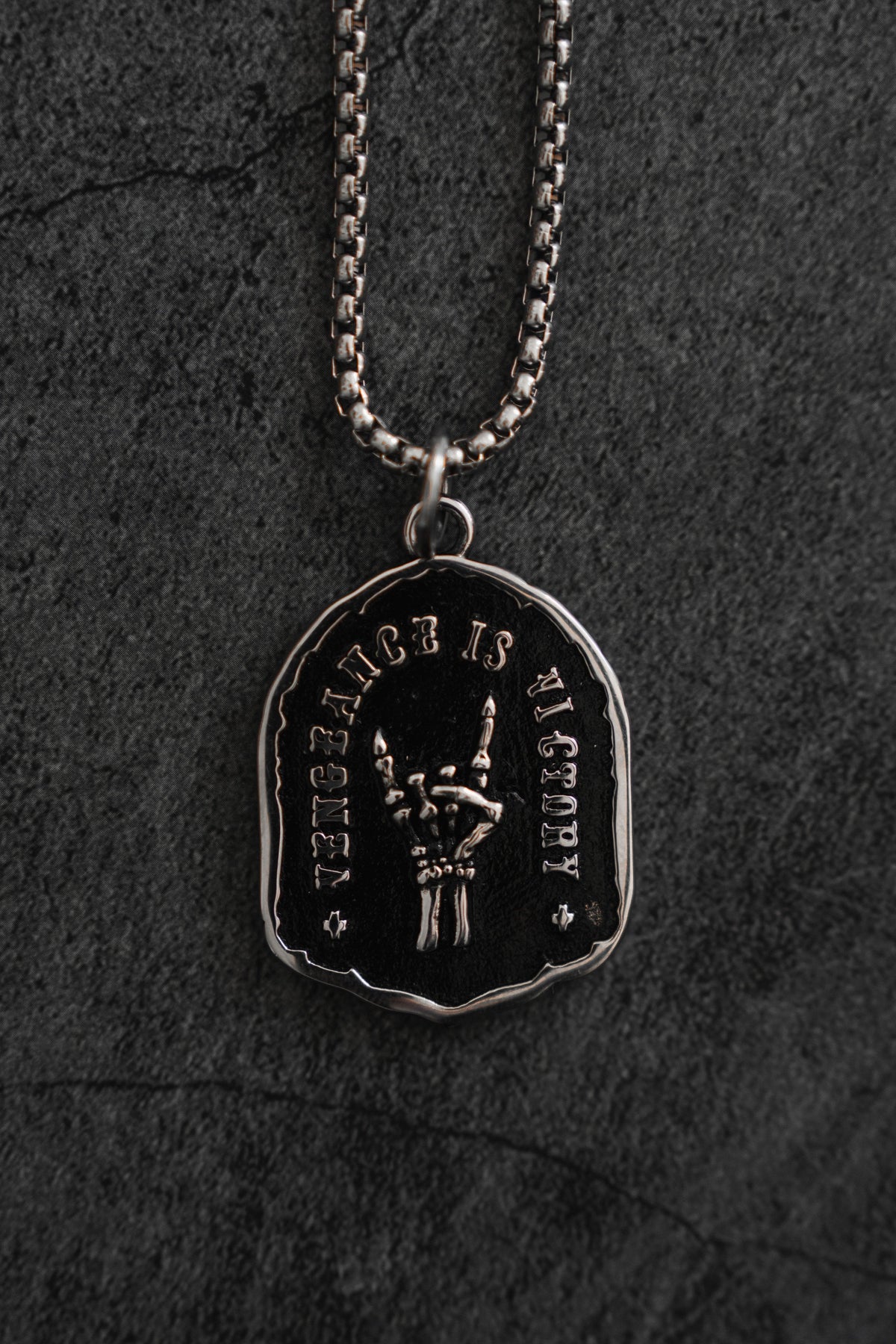 Vengeance Necklace: black shield-shaped pendant with skeletal hand and VENGEANCE IS VICTORY lettering, front product view.