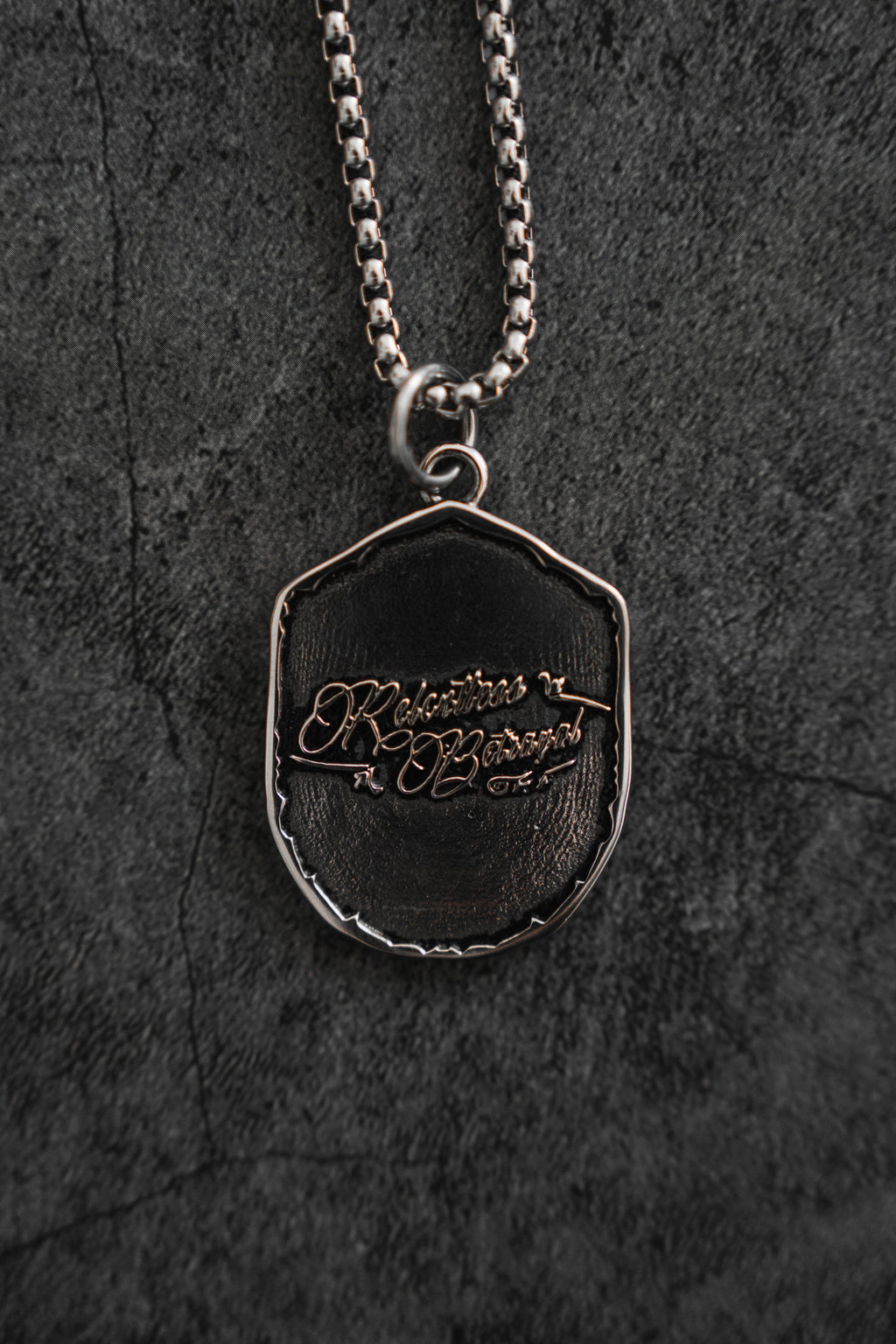 Vengeance Necklace: brand-script reverse on a shield-shaped pendant, reverse product view.