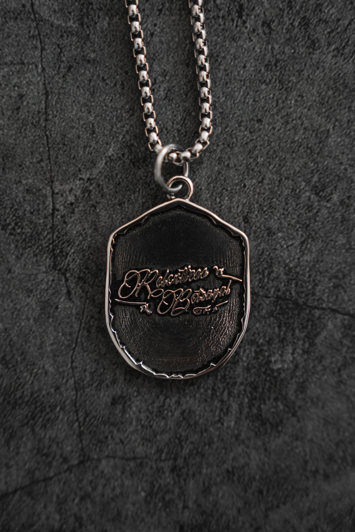 Vengeance Necklace: brand-script reverse on a shield-shaped pendant, reverse product view.
