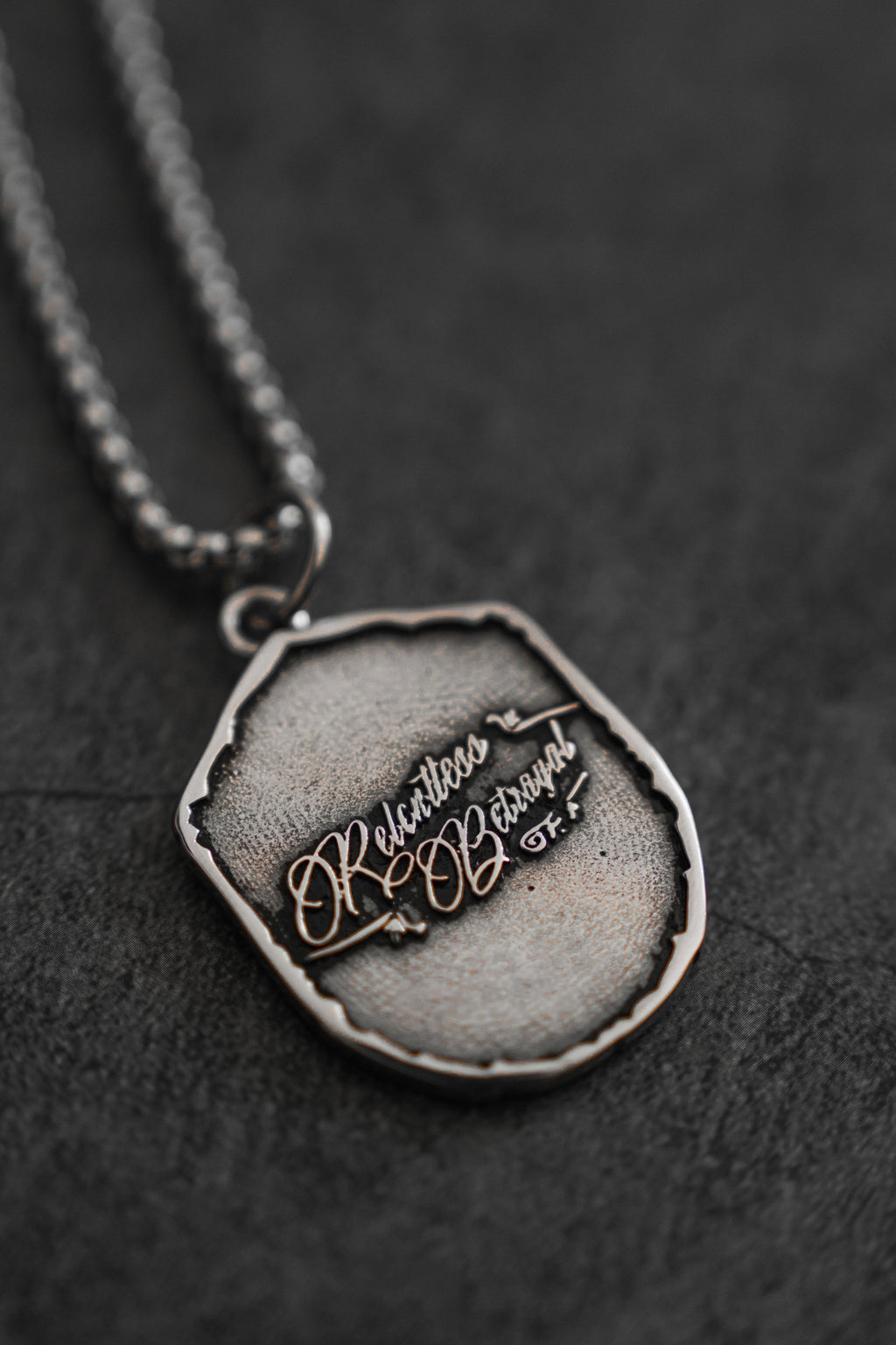 Vengeance Necklace: brand-script reverse on a shield-shaped pendant, angled reverse view.