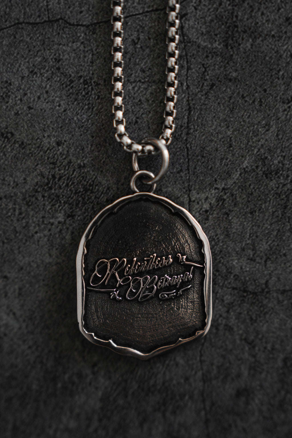 Vengeance Necklace: brand-script reverse on a shield-shaped pendant, reverse with chain.