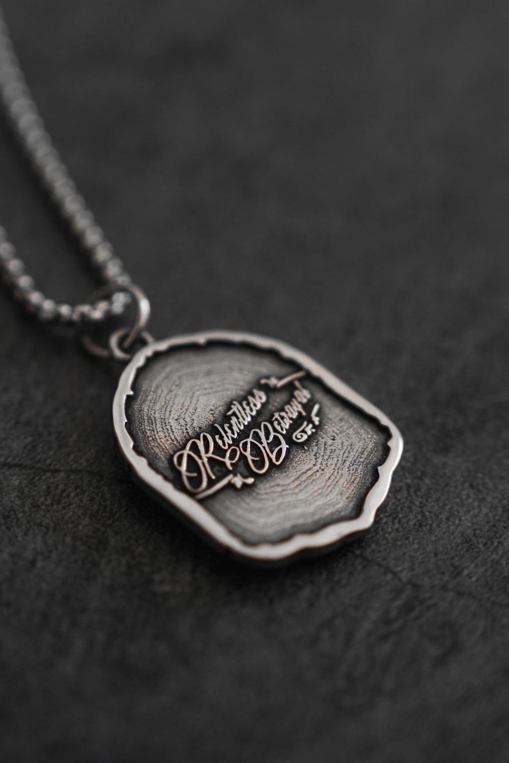 Vengeance Necklace: brand-script reverse on a shield-shaped pendant, angled reverse view.