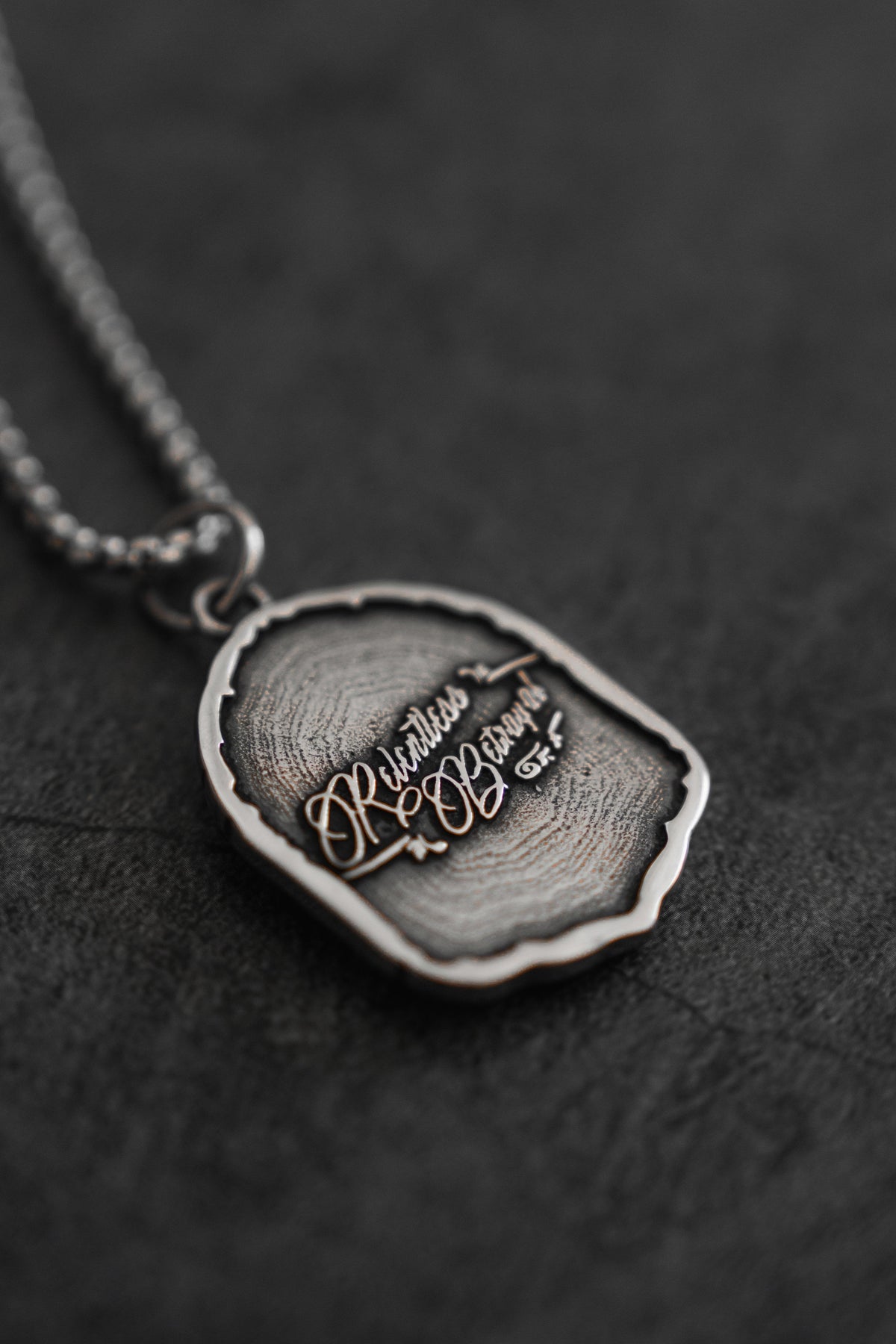 Vengeance Necklace: brand-script reverse on a shield-shaped pendant, angled reverse view.