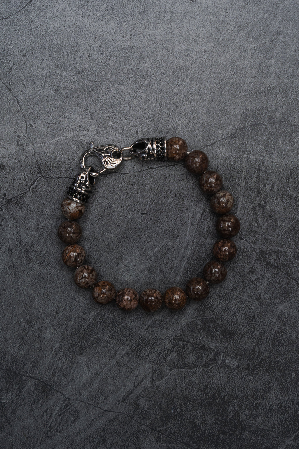 The Black Seal Bracelet: brown speckled round beads with decorative silver-tone clasp, full bracelet on gray surface.