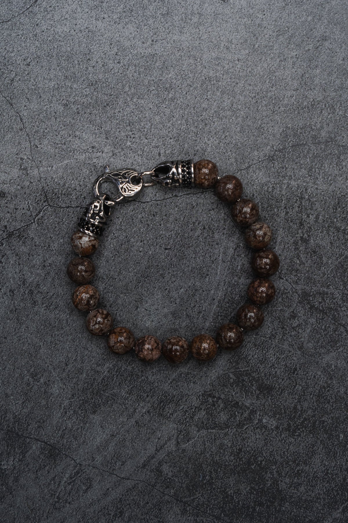 The Black Seal Bracelet: brown speckled round beads with decorative silver-tone clasp, full bracelet on gray surface.