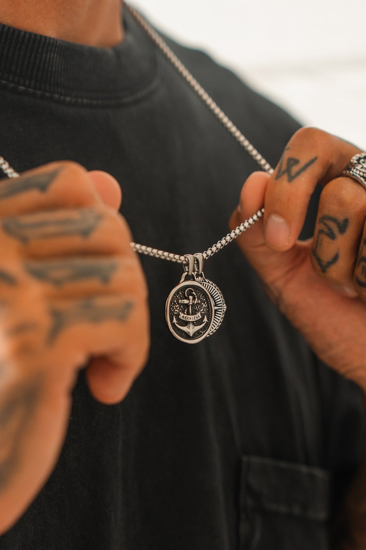 Reckless Soul Necklace: paired round anchor and compass-rose pendants on a silver-tone chain, held against a shirt.