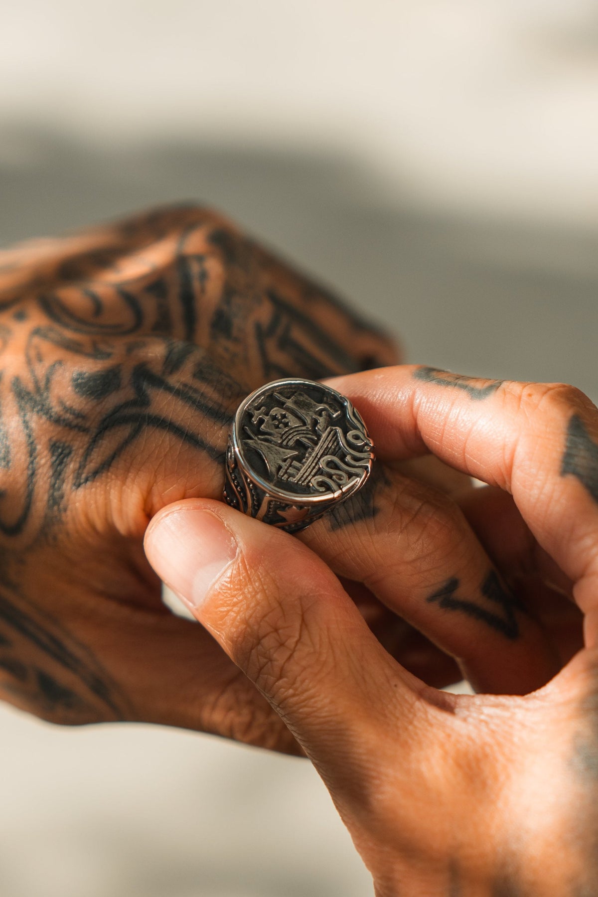 The Rise of the Kraken Ring: round signet face with a sailing ship and curling tentacles, being adjusted on a finger.
