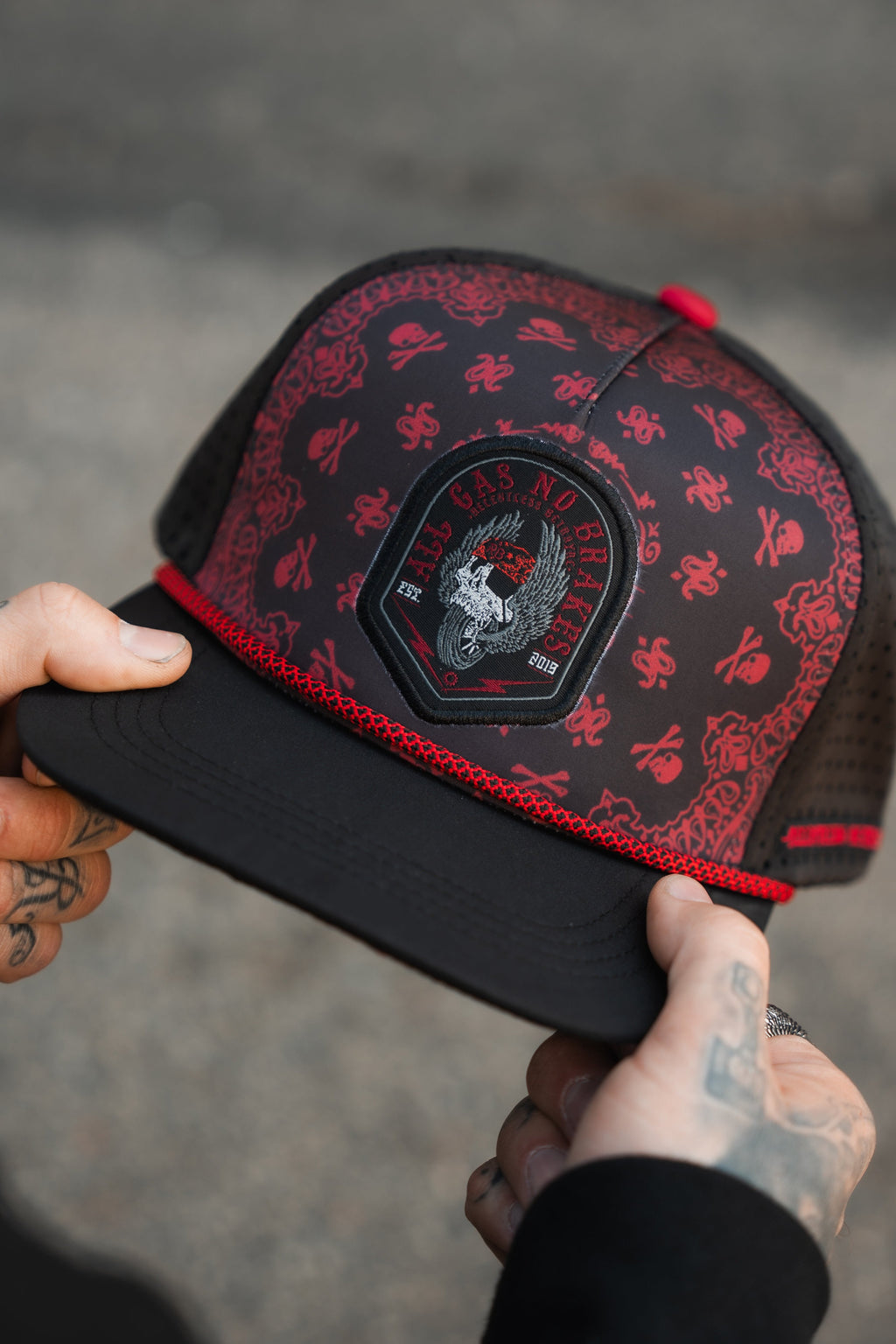 All Gas No Brakes Premium Snapback: black cap with red bandana-style print, skull patch and red rope trim, held in hands.