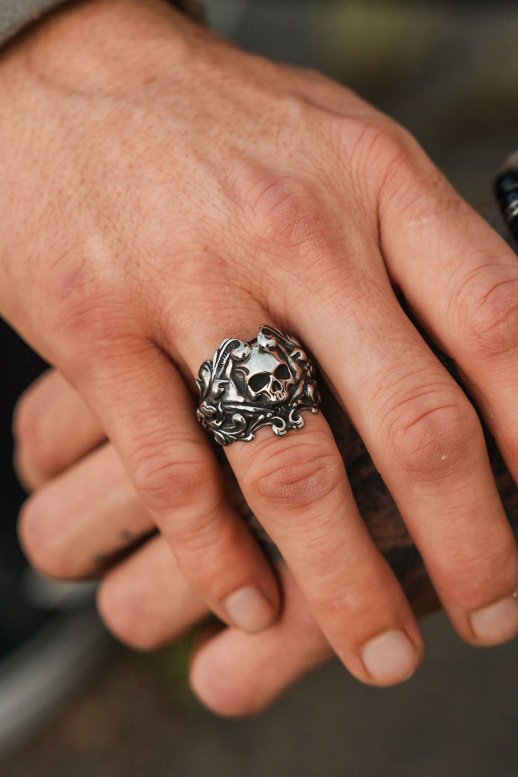 Gravewater Ring: sculpted skull with ornate curling side details, close-up on a hand.