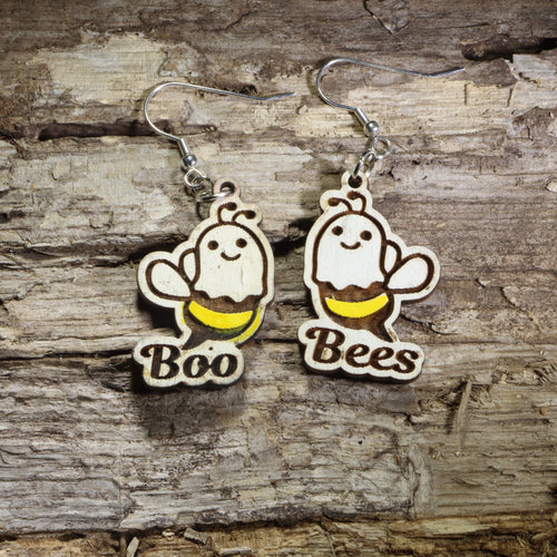 Wooden ghost-bee earrings reading 'Boo' and 'Bees', hand-painted with yellow stripes, on a wood-grain surface