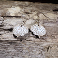 Wood-etched brain silhouette earrings hanging from silver fishhook wires, on a weathered wood-grain surface