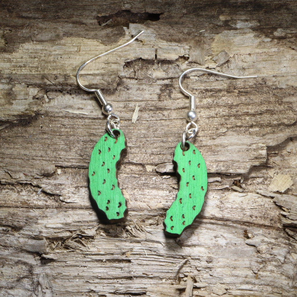 Green pickle-shaped wooden earrings with dot detailing, on a wood-grain surface
