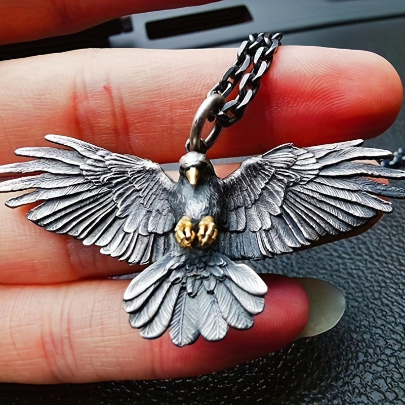 Falcon pendant with wings spread, dark oxidized finish, held in a hand on a metal chain