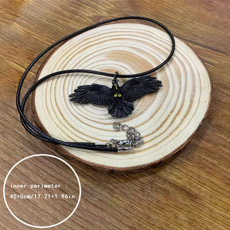Falcon pendant on a black cord necklace with a lobster clasp, coiled on a wood slice