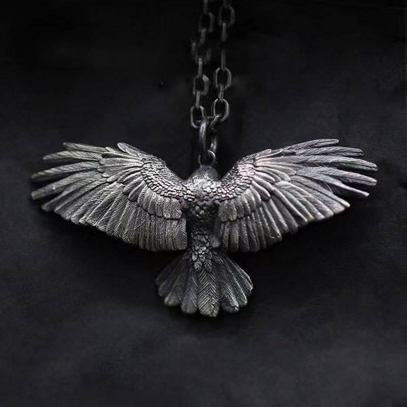Falcon pendant with wings spread on a metal curb chain, shown against a dark background