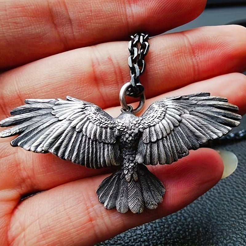 Close-up of the falcon pendant's wings and feather detail, dark oxidized finish, held in a hand