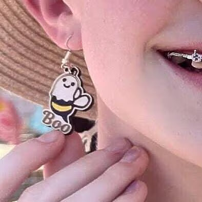 Wooden 'Boo' ghost-bee earring worn on a model's ear, close-up view