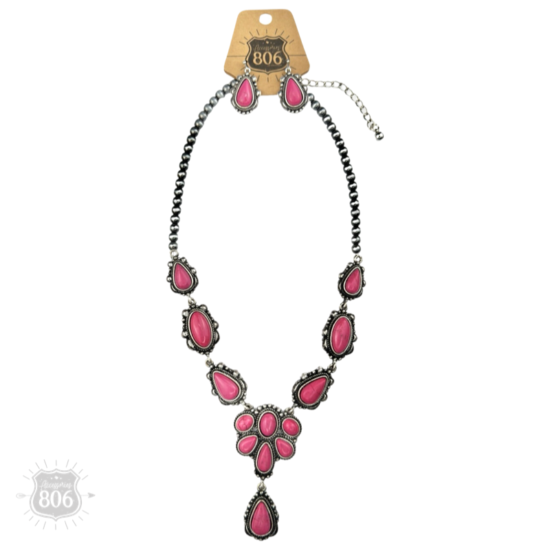 Fuchsia-pink concho necklace and matching earrings on a wood background, showing the teardrop and oval stone clusters