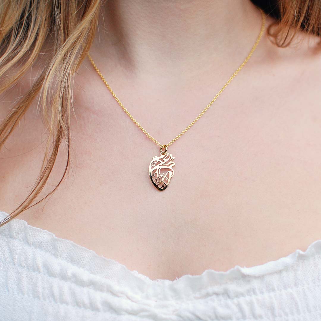 Model wearing a gold anatomical heart pendant necklace at the collarbone