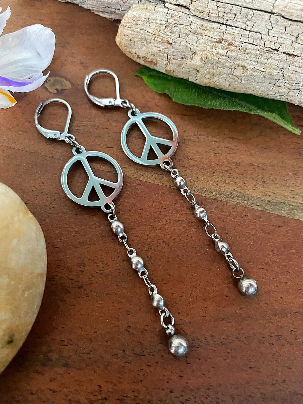 Pair of Peace Sign Drop Earrings laid flat, showing the silver-tone peace sign charm and beaded chain drop