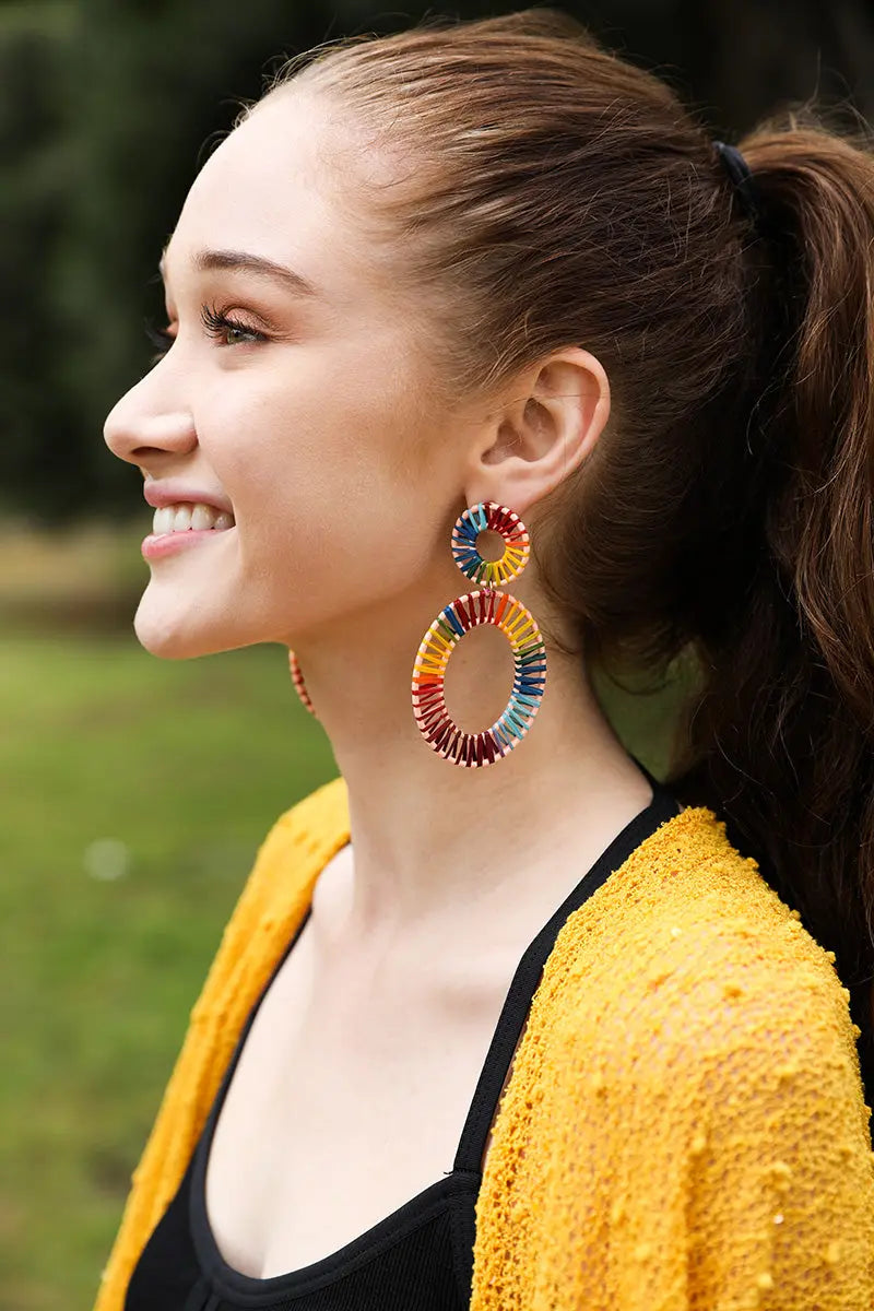 Model wearing the Rainbow Raffia Hoop Earrings in profile, smiling, paired with a yellow cardigan